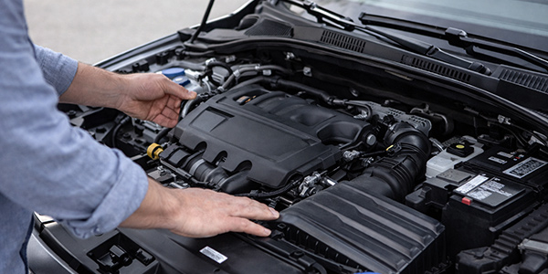 Hände öffnen Motorhaube und prüfen Motorraum bei Gebrauchtwagenbesichtigung