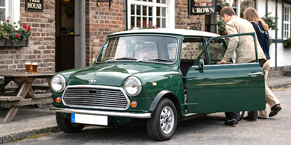 Klassischer Mini in British Racing Green vor einem Pub, zwei Personen steigen ein.