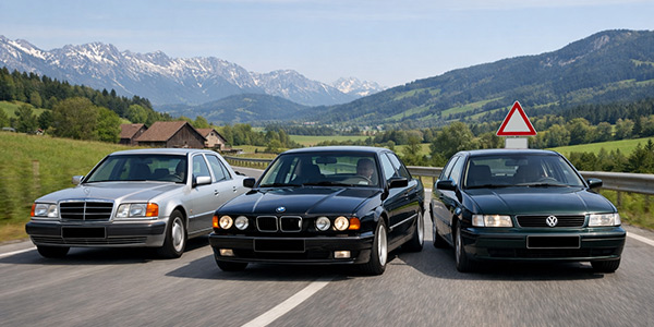 90er‑Jahre‑Oldtimer wie Mercedes W124, BMW E34 und VW Passat B4 auf einer österreichischen Landstraße.