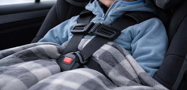 Kind im Kindersitz mit dünner Winterkleidung und korrekt angelegtem Gurt.